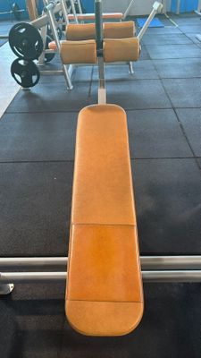 a bench in the middle of a gym with a row of chairs in the background