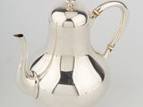 a silver coffee pot with a handle and a handle on a white surface