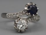 une photo d'une bague sertie d'un diamant et d'un saphir posée sur une surface grise