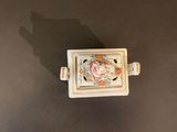 an overhead view of a small square ceramic object on a black surface