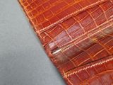 crocodile skin wallet with a metal clasp on a gray surface