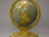 an old yellow and green globe on a wooden stand on a gray background