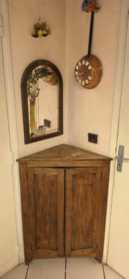 a small corner cabinet with a mirror on the wall