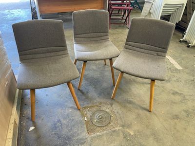 trois chaises grises posées sur un sol en ciment, près d'un mur