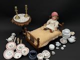 une poupée assise sur un lit, entourée d'autres objets