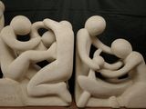 two sculptures of a man and a woman holding hands on top of a wooden table