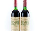 two bottles of red wine sitting next to each other on a white surface