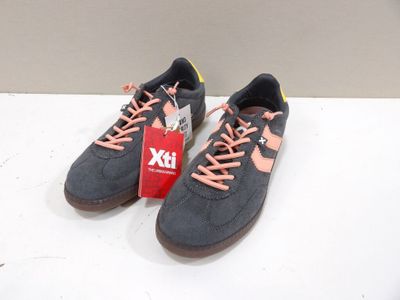Des baskets grises et orange avec des lacets roses sont posées sur une surface blanche