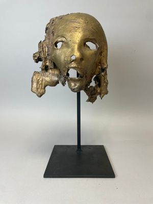 a bronze mask on a black stand with a white background