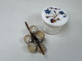 un petit récipient blanc orné de fleurs bleues, à côté d'une grappe de raisin