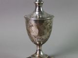 silver plated urn with lid on pedestal on grey background