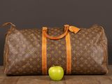 an apple sits next to a louis vuittou bag on a wooden table
