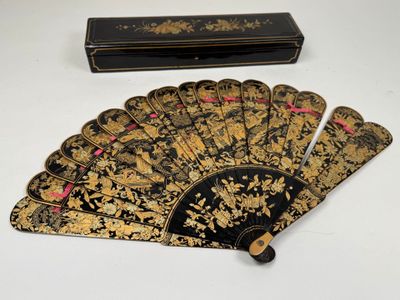 un vieil éventail noir et doré et son étui, posés sur une table blanche