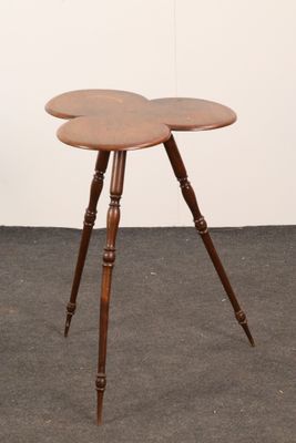 une petite table en bois à trois pieds, dont le plateau a la forme d'une fleur