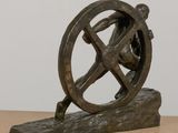 bronze sculpture of a man pushing a wheel on a wooden base