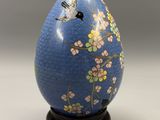 an egg with a bird and flowers painted on it sitting on a stand