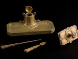 a gold inkwell with a pen and a knife next to it