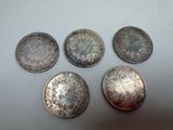 five silver coins are arranged on a white surface
