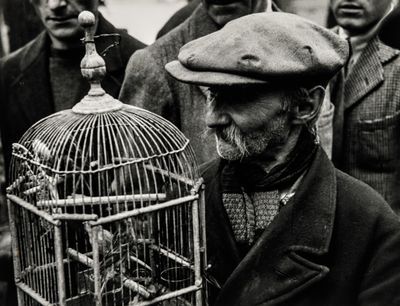 black and white photo of a man holding a bird in a cage