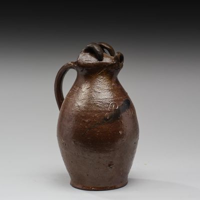 une image représentant un vase marron muni d'une anse, posé sur une surface blanche