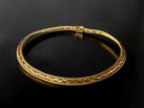 a gold bangle with intricate design on a black surface