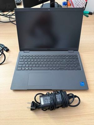 un ordinateur portable ouvert posé sur un bureau en bois, à côté d'un chargeur