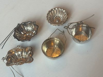 six passoires à thé en argent sont alignées sur une surface blanche