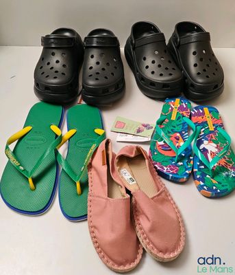 Plusieurs paires de sandales et de pantoufles sont alignées sur une table