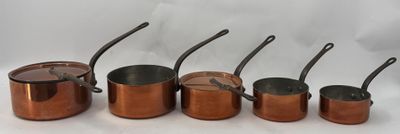 six casseroles et poêles de couleur cuivrée alignées sur un plan de travail blanc
