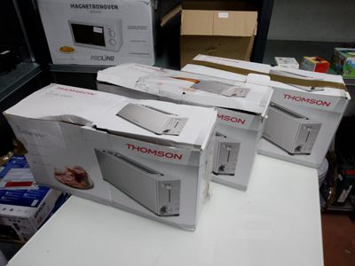 Quatre boîtes de micro-ondes sont empilées sur une table dans une pièce.