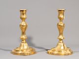 paire de bougeoirs anciens en laiton posés sur un socle, sur fond gris