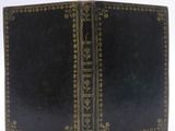 an old book with a black cover and gold trim on it