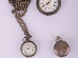 trois montres de poche anciennes et une chaîne posées sur un fond blanc
