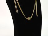 collier composé d'une chaîne en or et d'une pierre verte, présenté sur un mannequin noir