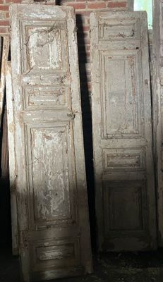 trois vieilles portes posées dans une pièce, près d'un mur de briques