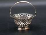 an antique silver basket with a handle on a black surface