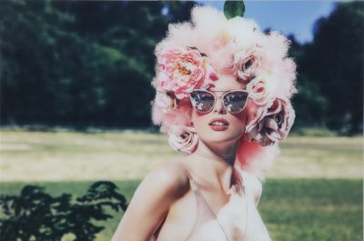 une femme portant une perruque rose et des lunettes de soleil, en train de poser pour une photo