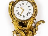 une horloge en or accrochée au mur, surmontée d'une couronne