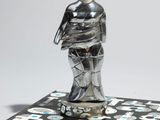 une figurine en argent posée sur un carrelage noir et blanc