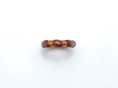 une image représentant une bague rouge et dorée posée sur une surface blanche