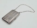 un porte-monnaie argenté entouré d'une chaîne, posé sur une surface blanche