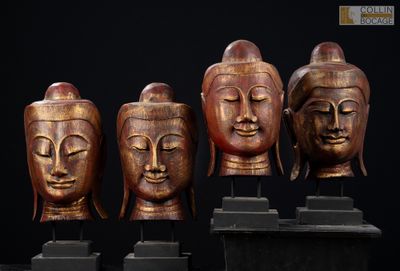 quatre têtes de Bouddha en bois posées sur des socles, sur fond noir