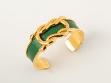 a close up of a gold and green bracelet on a white surface