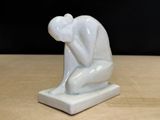 a white statue of a man sitting on a wooden table