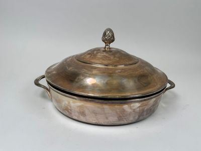 une cocotte ancienne en métal argenté avec un couvercle, posée sur un plan de travail blanc