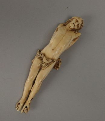 une figurine en ivoire représentant Jésus sur la croix, posée sur une surface grise