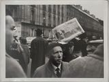photographie en noir et blanc d'un homme tenant un journal au milieu d'une foule