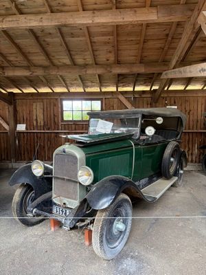 une vieille voiture verte dans un garage au toit en bois