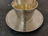 a silver cup and saucer sitting on a table