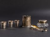 cinq tasses en argent et une cuillère en argent posées sur une table